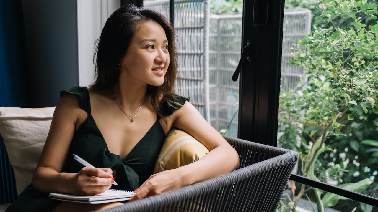 A woman sitting with a notebook looking out to her garden deciding whether to pick coaching or counselling